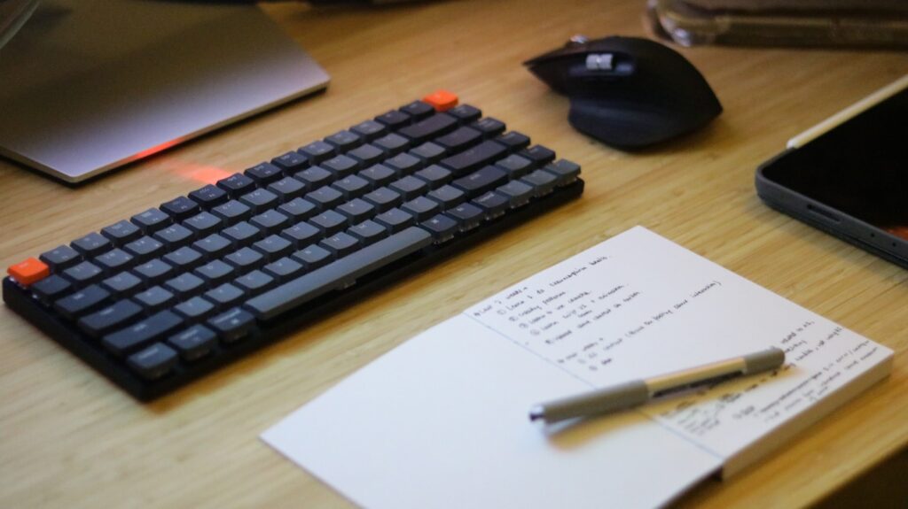 a desk with a keyboard, mouse, cell phone and notepad, ready to Nail how much to charge for landing page copy!
